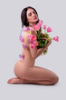 Studio portrait of a naked beautiful sexy slim young caucasian brunette girl covered with pink butterflies holding a tulips bouquet sitting on the floor attractively posing with dreamily closed eyes