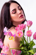 Close-up studio portrait of a naked beautiful sexy slim young caucasian brunette girl covered with pink butterflies holding a tulips bouquet attractively posing with dreamily closed eyes