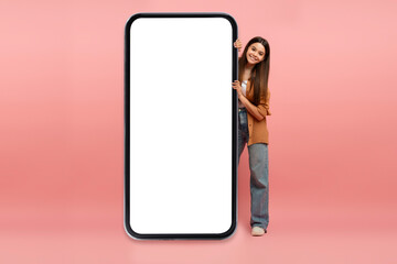 Wall Mural - Beautiful Teen Girl Peeking Out Behind Huge Blank Smartphone With White Screen