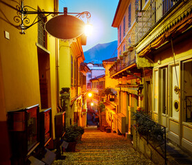 Bellagio village at lake Como near Milan Italy, region Lombardy. Famous street with paving stones stairs and cosy restaurants during sunrise glowing lanterns on old houses walls