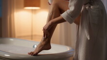 Slim Model Moisturizing Legs Bathroom Closeup. Unknown Lady Applying Skin Lotion