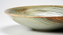 Closeup Of A Glazed Stoneware Bowl With A Streaked Design In Shades Of Soft Green, Brown, And Grey. The Glaze Adds A Subtle Shine To The Bowl, While The Natural Variations In The Clay Give