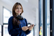 © David - Young adult happy smiling Hispanic Asian student wearing headphones standing indoor using digital tablet in university campus or at virtual office. College female student learning remotely.