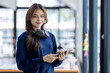 © David - Young adult happy smiling Hispanic Asian student wearing headphones standing indoor using digital tablet in university campus or at virtual office. College female student learning remotely.