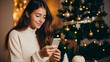Young woman in a white sweater orders New Year's gifts during the Christmas holidays at home, using a smartphone and a credit card.