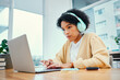 © Rene L/peopleimages.com - Headphones, laptop and young woman typing for research in living room listening to music, playlist or album. Technology, computer and female person from Colombia streaming song on radio for studying.