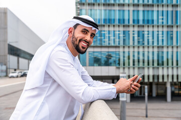 Wall Mural - Arab middle-eastern man wearing emirati kandora traditional clothing in the city - Arabian muslim businessman strolling in urban business centre.