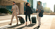 © N F/peopleimages.com - Business people, team walking and travel with suitcase in city for corporate, job opportunity and networking. Professional woman and men talking at outdoor hotel or on the way to airport with luggage