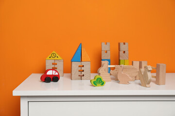 Poster - Set of wooden toys on white chest of drawers near orange wall, space for text. Children's development