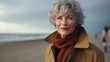 Mature stylish senior woman in a coat on the beach coast spending active retirement and happy aging while travelling around the world leading active lifestyle