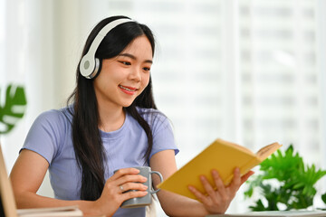 Young woman in headphone reading book, enjoying leisure weekend time at home