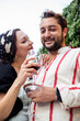Portrait of a young couple in love enjoying a glass of red wine on a rooftop terrace, looking to each other and smiling