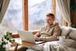 Man Smiling at Laptop in Cozy Cabin with Mountain View