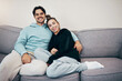 © Rene L/peopleimages.com - Portrait, relax and smile with a couple on a sofa in the living room of their home together for bonding. Love, hug or date with a happy man and woman in their apartment for romance or relationship