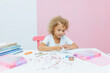 © inna717 - Cute little blonde girl making bead jewelry at a table in the room