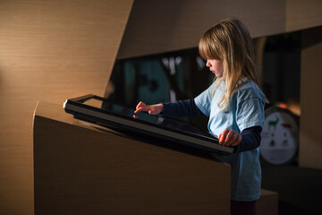 Primary school girl using big touch screen display and delighted looking around. Children and modern technology concepts.