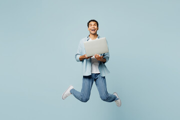 Wall Mural - Full body young IT man of African American ethnicity he wearing shirt casual clothes jump high hold use work on laptop pc computer isolated on plain pastel light blue cyan background studio portrait.