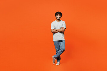 Wall Mural - Full body young smiling cheerful satisfied happy Indian man he wears t-shirt casual clothes hold hands crossed folded look camera isolated on orange red background studio portrait. Lifestyle concept.