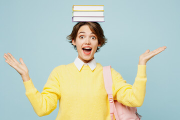 Wall Mural - Young excited surprised woman student wear casual clothes yellow sweater backpack bag hold stack of books on head look camera isolated on plain blue background. High school university college concept.