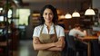 Happy Hispanic female chef smiling and  doing arm crossed gesture confidently in the restaurant.