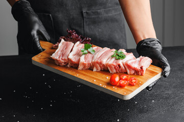 Wall Mural - Butcher woman hold wooden board with fresh meat pork ribs on dark background