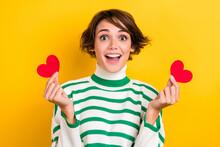 Photo of shiny excited lady wear striped pullover holding two small red hearts isolated yellow color background