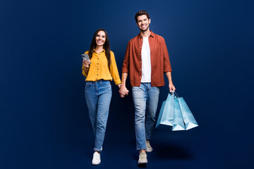 Canvas Print - Full body photo of two attractive people hold arms walk use smart phone carry mall bags isolated on blue color background