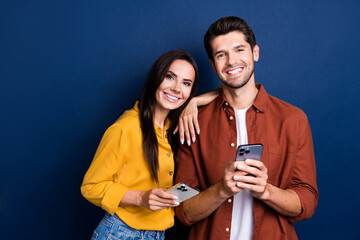 Wall Mural - Portrait of two positive idyllic partners embrace toothy smile use smart phone isolated on dark blue color background