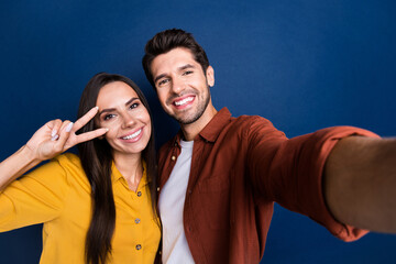 Sticker - Photo of lovely positive people toothy smile demonstrate v-sign near eye make selfie isolated on blue color background