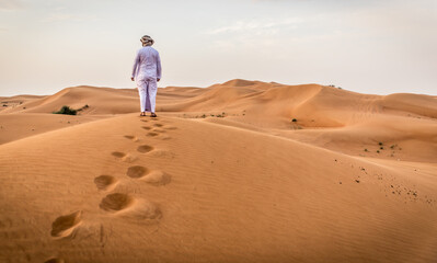 Wall Mural - Arabic man with traditional emirates clothes walking in the desert