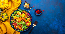 Healthy Autumn Pumpkin Salad With Lettuce, Arugula, Pomegranate Seeds And Walnuts. Comfort Slow Food. Blue Background. Top View
