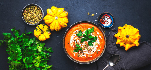 Wall Mural - Autumn pumpkin soup puree with pumpkin seeds, cream, pepper and parsley. Winter healthy vegan slow comfort food. Soup bowl on black table background. Top view