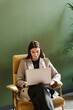 © muse studio - The SMM manager in the chair uses a laptop to pay for online goods in the website stores. The student is a happy person real estate agent. Beautiful office clothes jacket.