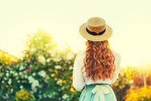 Art Photo Happy Woman Retro Lady In Vintage Straw Hat, Girl Long Curly Red Hair Old Style White Blouse Mint Skirt Dress Back Rear View. Fairy Tale Girl Enjoy Green Tree Sun Light Sky Summer Nature