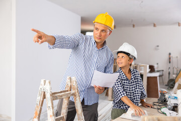 Wall Mural - Father and son in helmets talking about space planning in new apartment. Man making pointing finger gesture.