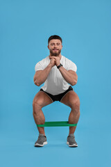 Wall Mural - Young man exercising with elastic resistance band on light blue background