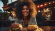 A happy woman eating a burger in an outdoor restaurant as a Breakfast meal craving deal.