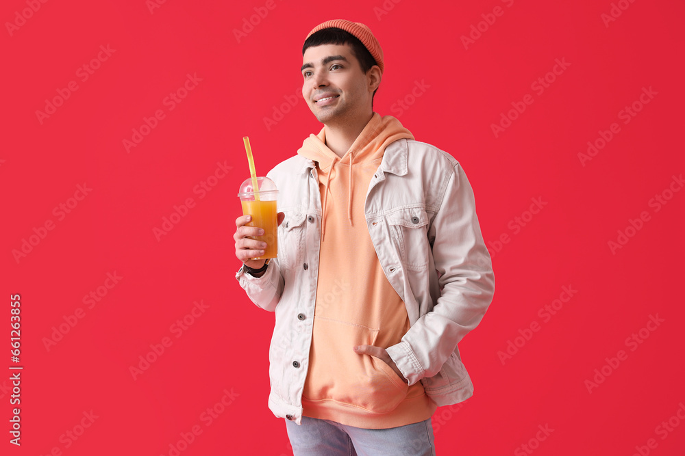 Stylish young man with glass of beverage on red background