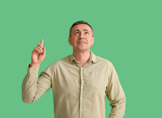 Canvas Print - Mature man in shirt pointing at something on green background