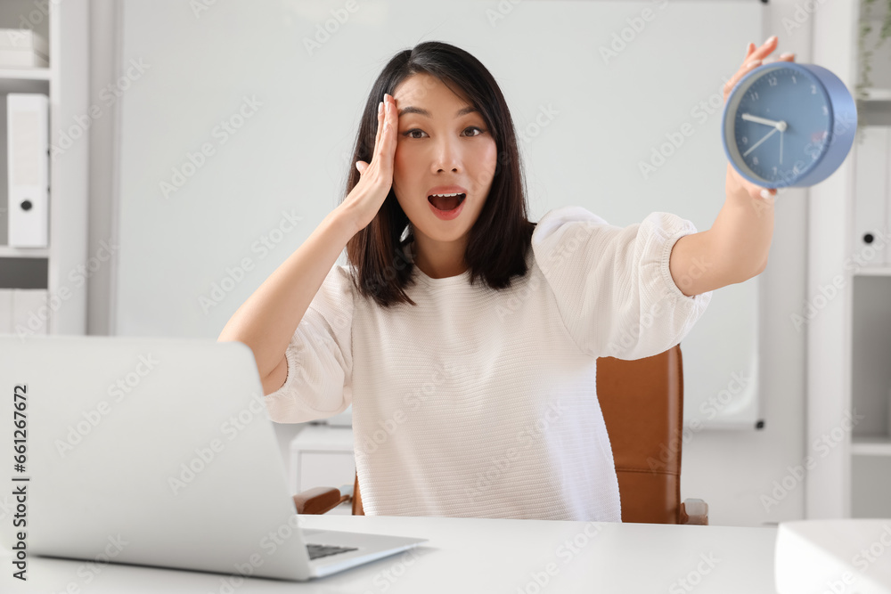 Surprised Asian woman with alarm clock in office