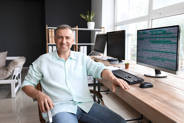 Mature male programmer sitting in light office at his workplace