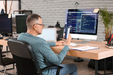 Mature male programmer with mobile phone working in office