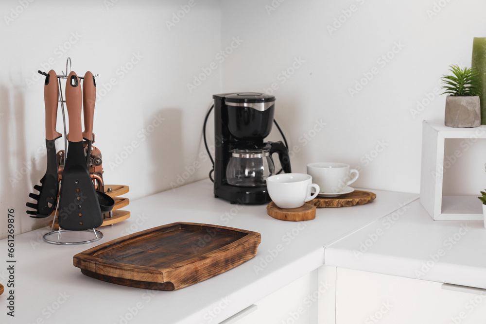 White kitchen counter with cutting board, coffee machine, cups and utensils