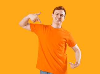 Wall Mural - Young man pointing at his orange t-shirt on yellow background