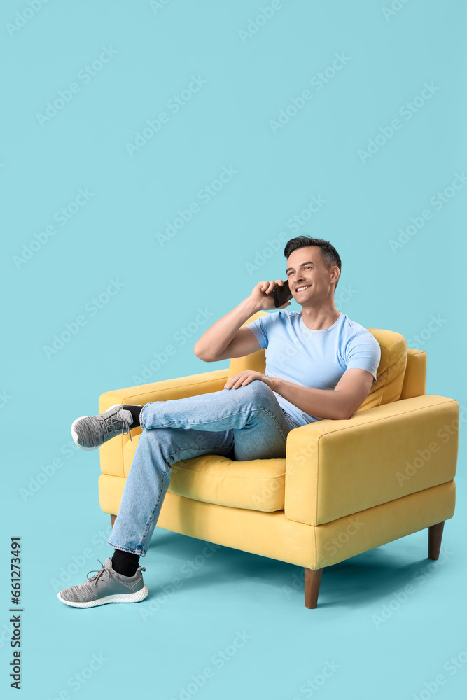 Handsome man talking by mobile phone in yellow armchair on blue background