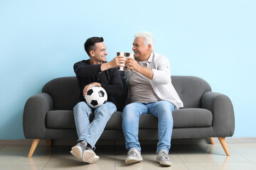 Wall Mural - Young man with his father watching football game on sofa near blue wall