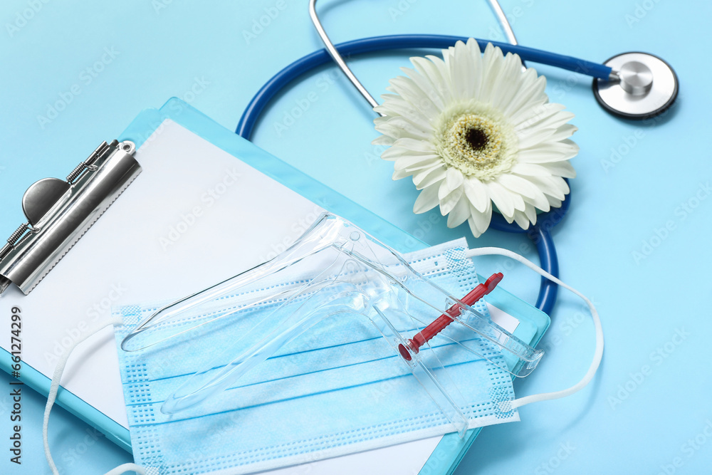 Gynecological speculum, mask, stethoscope and clipboard on blue background