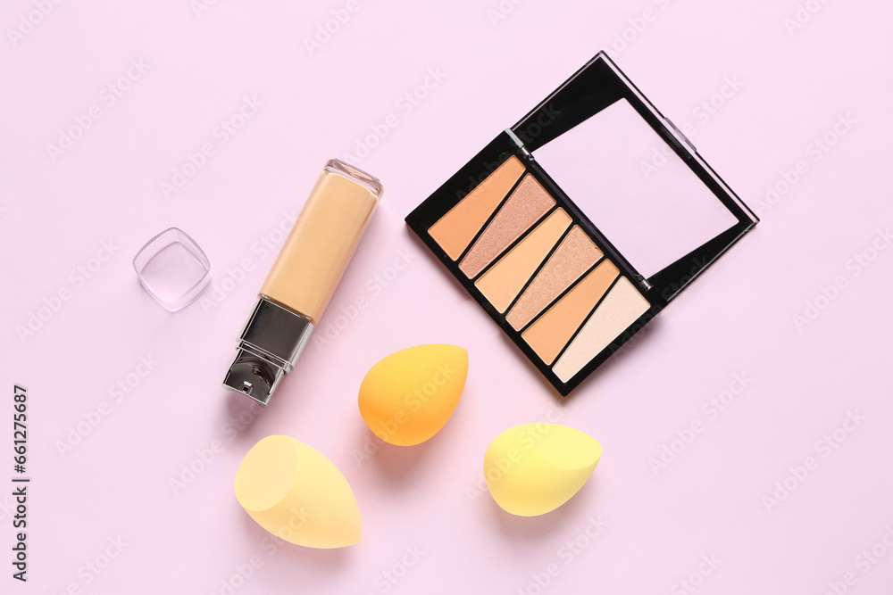 Bottle of liquid foundation, eyeshadows and makeup sponges on lilac background