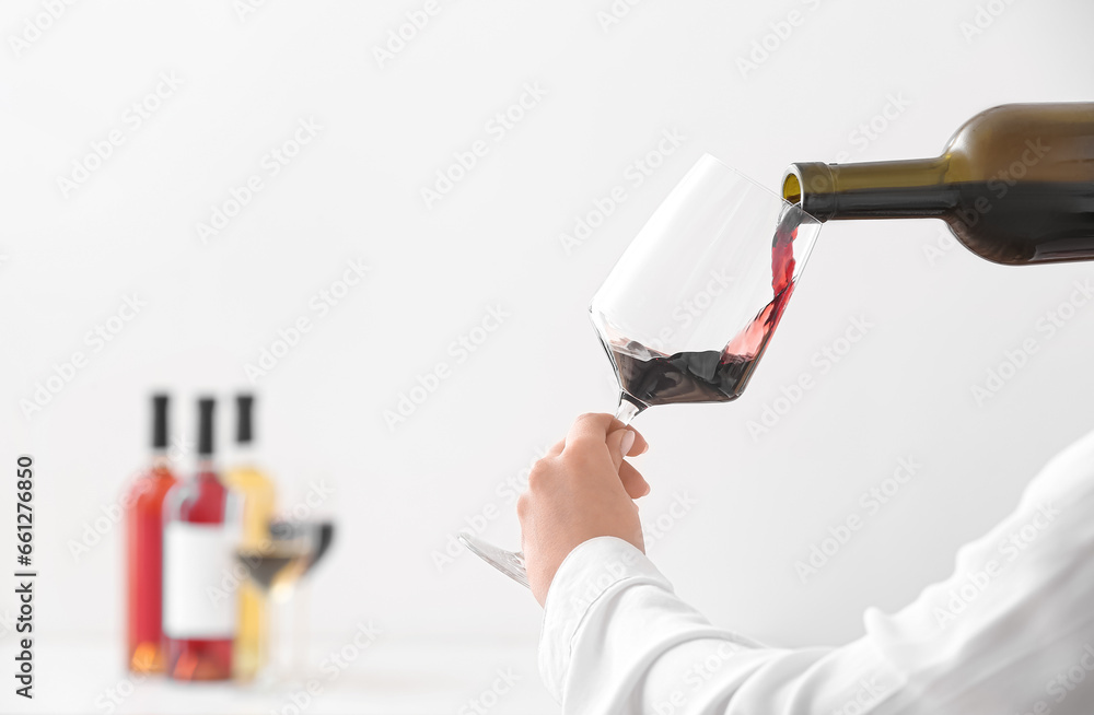 Woman pouring exquisite red wine from bottle into glass on light background