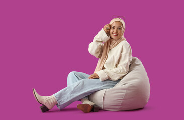 Sticker - Young Muslim woman sitting in beanbag on purple background